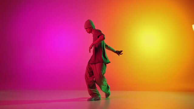 Talented break-dancer dancing in motion in neon light against gradient pink-yellow background. Concept of hobby, sport, creativity, fashion and style, motion, action. Ad