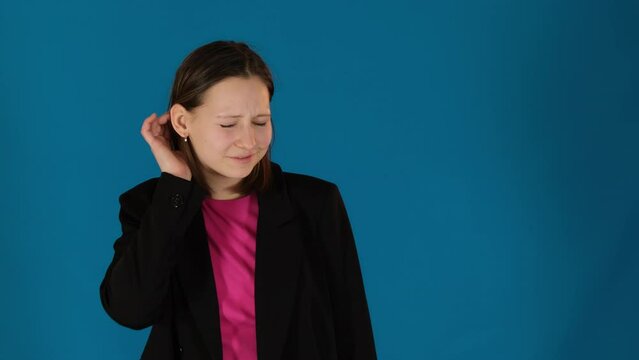 Young woman eavesdrops gossip putting hand close to ear. Surprised lady in jacket makes zip mouth gesture on blue background