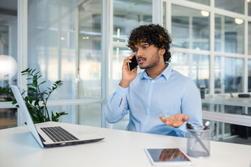 Young Hispanic businessman looking frustrated and angry during a phone call in a modern office...
