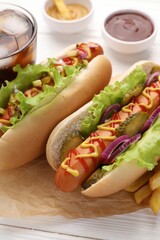 Delicious hot dogs with lettuce, onion and pickle on white wooden table, closeup