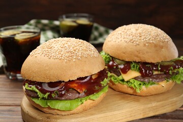 Board with delicious cheeseburgers on wooden table, closeup