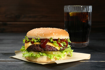 Burger with delicious patty and soda drink on black wooden table