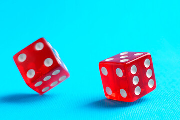 Two red game dices falling on light blue background, closeup