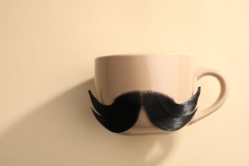 Artificial moustache and cup on beige background, top view