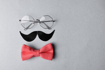 Man's face made of artificial mustache, bow tie and glasses on light grey background, top view....