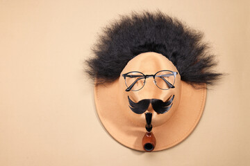 Man's face made of artificial hair, mustache, glasses and hat on beige background, top view. Space...