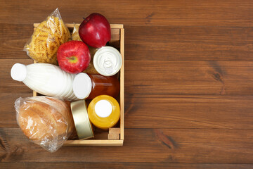 Humanitarian aid. Different food products for donation in crate on wooden table, top view. Space for text