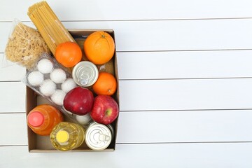Humanitarian aid. Different food products for donation in box on white wooden table, top view....