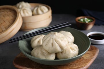 Delicious bao buns (baozi) in bowl and chopsticks on grey table, closeup