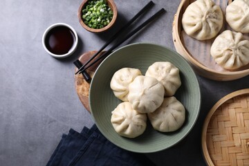 Delicious bao buns (baozi), chopsticks, soy sauce and green onion on grey table, flat lay