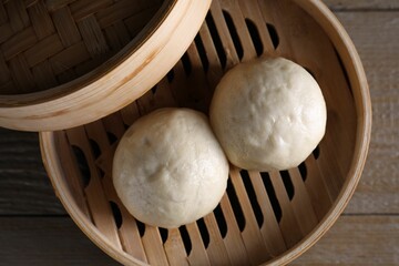 Delicious Chinese steamed buns in bamboo steamer on wooden table, top view