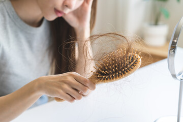 Problem hair, stressed beautiful asian young woman, girl hand holding comb show hairbrush with hair loss in brush after brushing fall near mirror at home. Health care, beauty with treatment concept.