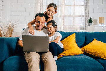 A family's quality time at home as parents and kids sit on the couch with a laptop. This modern...