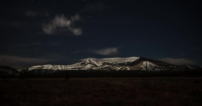 Snow capped mountains at night with rolling clouds