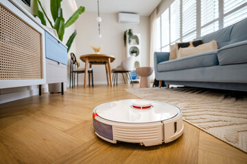Robotic vacuum cleaner cleaning wooden floor in living room
