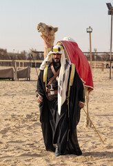 Saudi man in traditional clothing with his camel in a desert