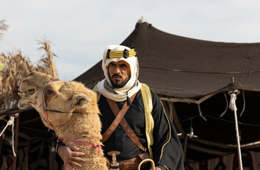 Saudi man in traditional clothing with his camel in a desert