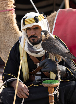 Saudi man in traditional clothing with his camel in a desert