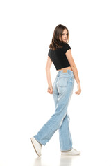 Young female model wearing ripped jeans and black shirt walking on a white background. Side,...
