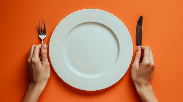 A woman holds cutlery over an empty plate against an orange background