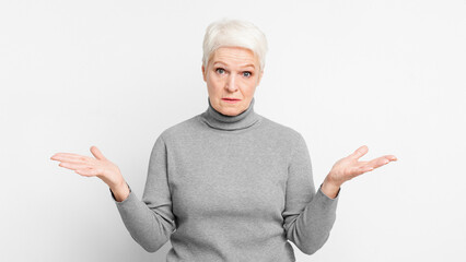 Perplexed senior woman with hands open on grey background