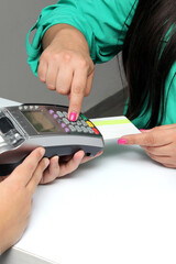 Latin adult woman with coffee in hand pays with a contactless credit card in a store and enters her...