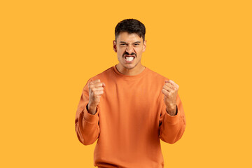 Annoyed man clenching fists in frustration against yellow background