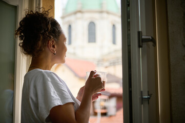 View from the back to a woman tourist holding a cup of aroma coffee, admiring the cathedral from...