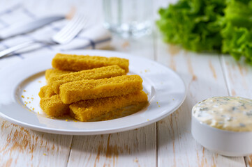 Tasty crispy deep fried fish fingers served with lemon and tartar sauce on wooden table.