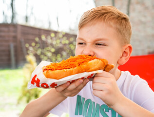 A boy eats a hotdog at a table in a cafe in a spring park