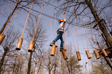 A boy in a helmet climbs a rope park in the spring