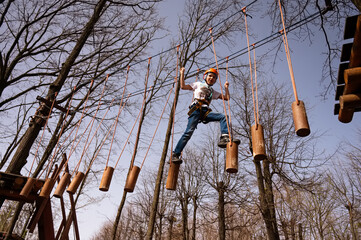 A boy in a helmet climbs a rope park in the spring