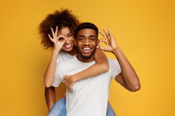 Young black couple piggyback ride, showing ok gesture