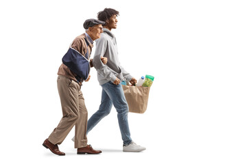 Young african american man helping a senior with a broken arm and carrying grocery bags