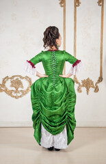 Beautiful woman in rococo style medieval dress standing near wall back pose