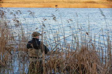 Obraz na płótnie Canvas Fisherman in waders catches pike in the lake