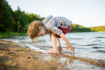 Cute little boy playing by a lake or river on hot summer day. Adorable child having fun outdoors during summer vacations.