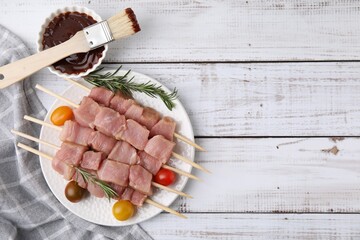 Skewers with pieces of raw meat, rosemary, tomatoes and marinade on rustic wooden table. Space for...