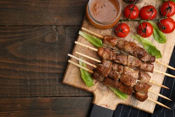 Tasty cooked marinated meat served with sauce and tomatoes on wooden table, flat lay. Space for text