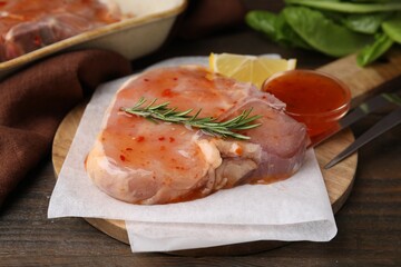 Board with raw marinated meat and rosemary on wooden table, closeup