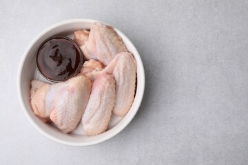 Plate with marinade and raw chicken wings on light textured table, top view. Space for text