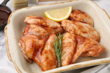 Raw marinated chicken wings, rosemary and lemon in baking dish on table, closeup