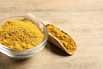 Curry powder in bowl and scoop on wooden table, closeup. Space for text