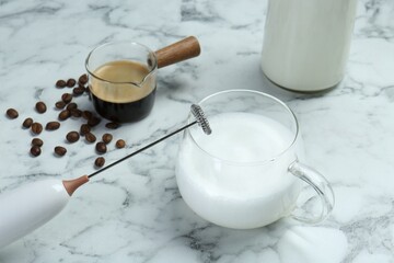 Mini mixer (milk frother), milk and coffee beans on white marble table, closeup