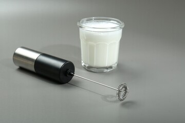 Mini mixer (milk frother) and whipped milk in glass on grey background