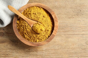 Dry curry powder in bowl and spoon on wooden table, top view. Space for text