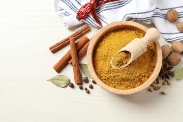 Dry curry powder in bowl and other spices on light wooden table, flat lay. Space for text