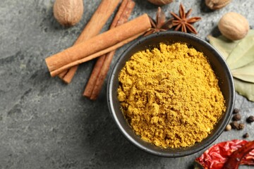 Dry curry powder in bowl and other spices on dark textured table, flat lay. Space for text