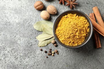 Dry curry powder in bowl and other spices on dark textured table, flat lay. Space for text