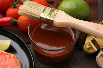 Tasty fish marinade, basting brush and products on wooden table, closeup